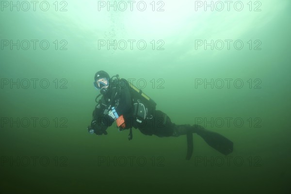 Diver underwater in greenish water with diving equipment during a safety stop. Dive site wreck of
