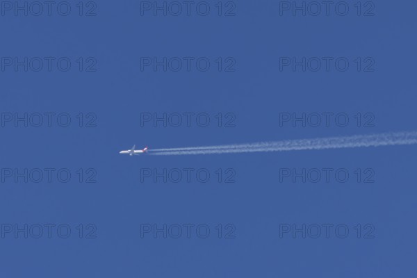 Jet passenger aircraft of Austrian Airways flying with vapour trails or contrails behind in a blue