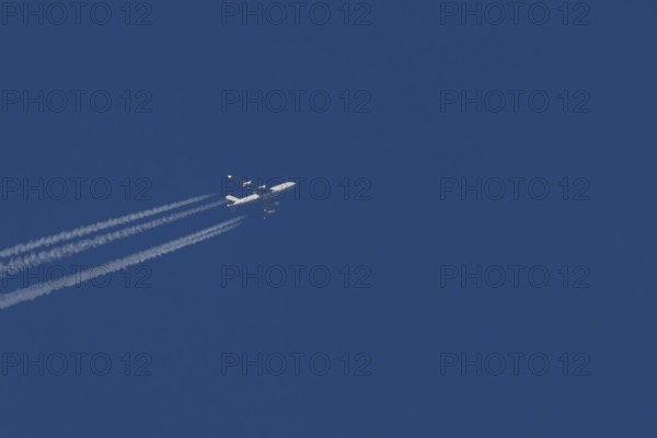 Boeing 747 Jumbo jet cargo aircraft in flight in a blue sky with vapour trails or contrails behind,