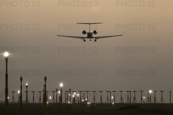 Executive business jet passenger aircraft landing over runway lights at sunset, London Stansted