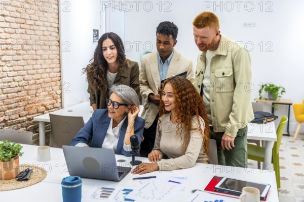 Diverse business team working together in a modern office, grouping around a laptop and microphone,