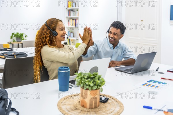 Two cheerful multiethnic customer service agents wearing headsets giving a high five, celebrating a