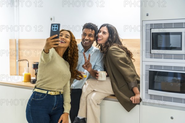 Diverse coworkers cheerfully taking a selfie on a smartphone during a relaxed office kitchen break,