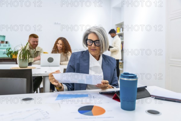 Mature female manager reviewing a financial report with charts and graphs on a table, collaborating