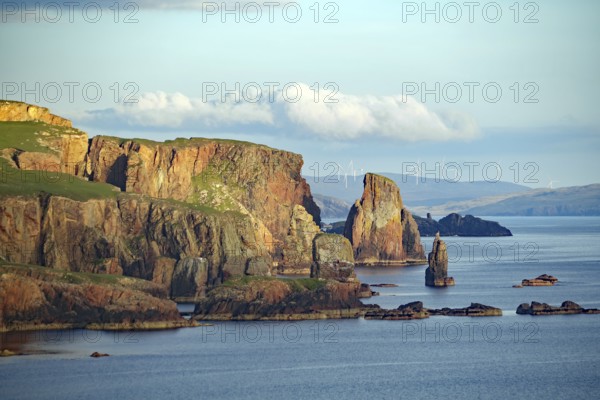 Cliffs and rock formations by the sea with wind turbines in the background, Eshaness, Shetland