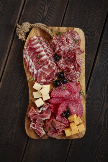 Assorted, sliced meat appetizer, prosciutto, salami and ham, with cheese and olives, on a wooden