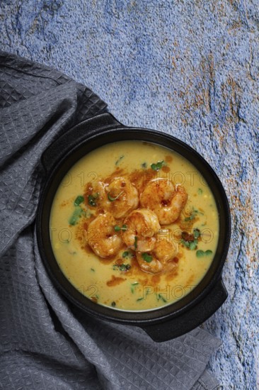 Creamy shrimp curry with spices, garnished with herbs, on a textured background, homemade, no