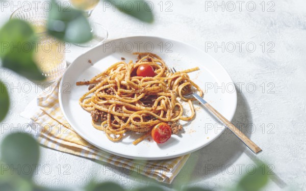 A plate of perfectly cooked spaghetti is topped with rich sauce and fresh tomatoes. Next to it, a
