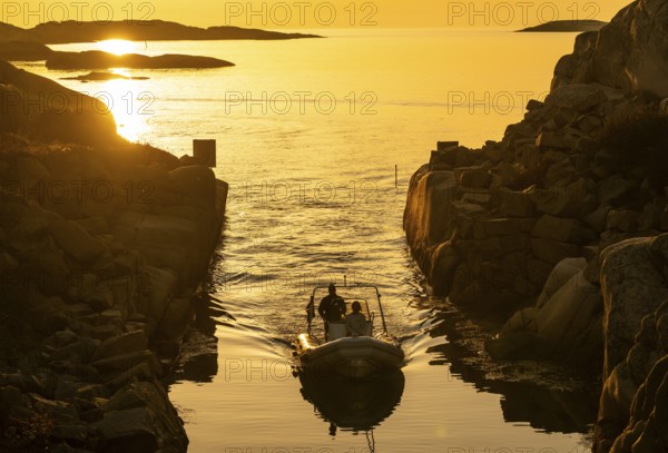 Motorboat with two persons sailing in harbour entrance at sunset, archipelago, Smögen,
