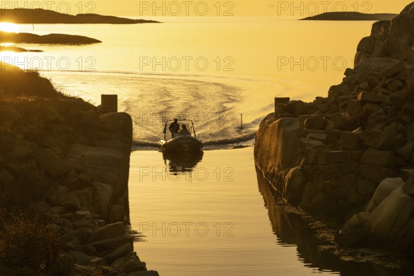 Motorboat with two persons sailing in harbour entrance at sunset, archipelago, Smögen,