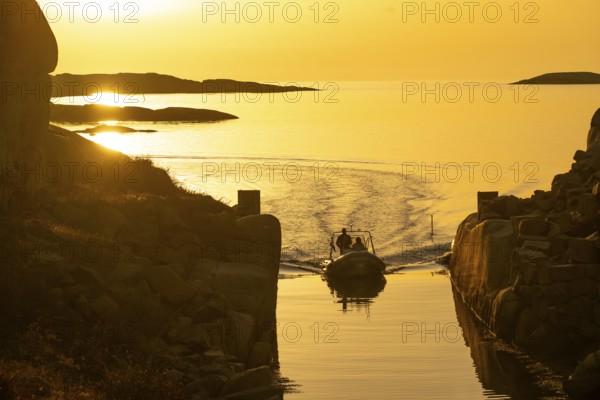 Motorboat with two persons sailing in harbour entrance at sunset, archipelago, Smögen,