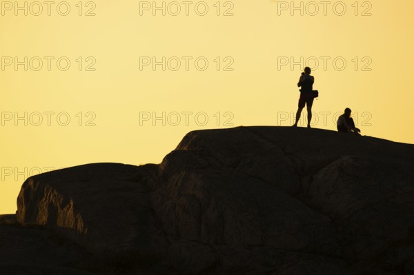 Silhouette of two tourists photographing the sunset on a rock, Smögen, Smögenbryggan, Västra