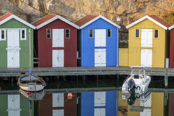Colourful boathouses and boats in the calm water in front of rocks in the harbour of Smögen,