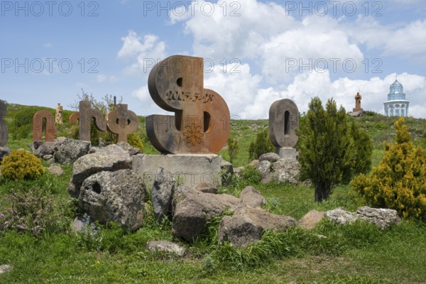 Stone sculptures in the shape of letters on a green meadow, surrounded by rocks and bushes under a