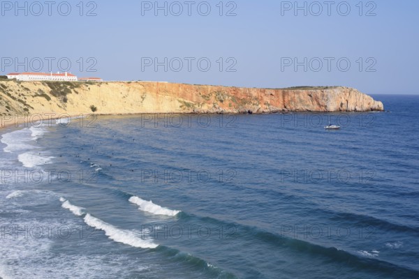 Cliffs with the Hotel Pousada de Sagres and surfers in the sea, Praia da Mareta, Sagres, Algarve,