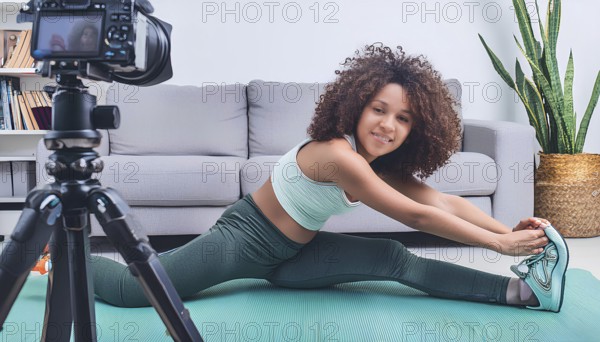 A young woman is stretching on a mat in front of a camera. The camera is on a tripod and is