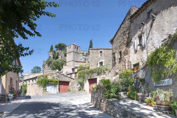 The sunlit village street of Moureze is lined with traditional stone houses with reddish-brown