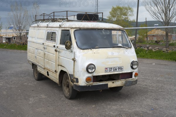 An old white van parked on the side of the road in a rural area, rust decoration visible, van,