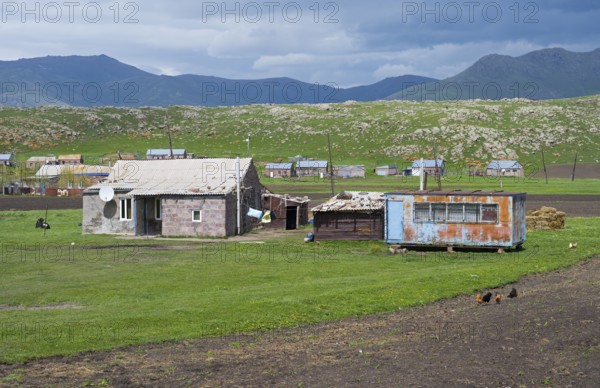 Rustic barns and buildings on green pasture against a mountainous backdrop with clouds in the sky,
