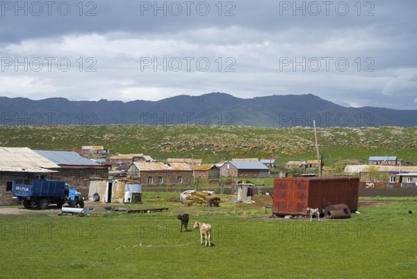 Rural settlement with huts and animals on a green pasture surrounded by mountains under a cloudy
