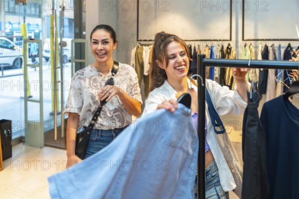Two joyful female customers laughing and enjoying the experience of searching for trendy clothes in