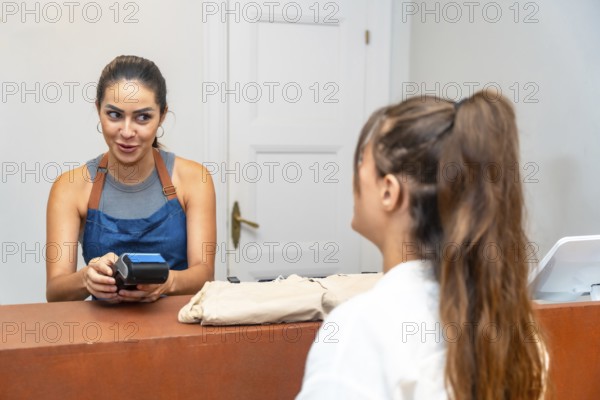 Smiling shop assistant holding a pos terminal for a customer making a contactless payment in a