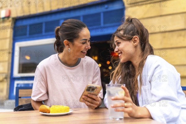 Two women are enjoying a meal and drinks at an outdoor cafe, sharing a moment of connection as they