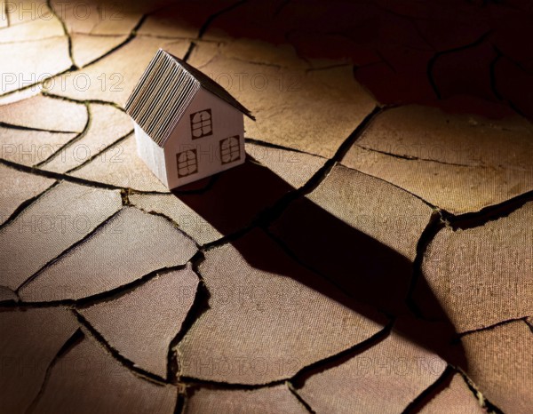 A cardboard miniature house placed on cracked, dry soil, illustrating drought, environmental
