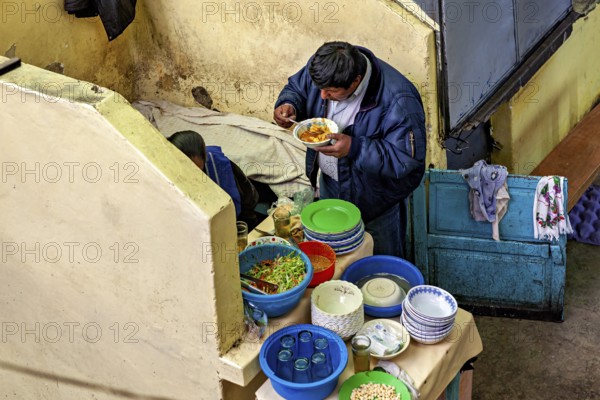 A man eats in a cosy corner with colourful crockery and a laid table, A man eats at a market stall