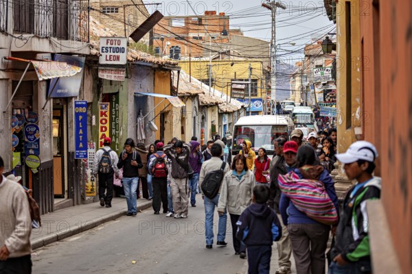 Lots of hustle and bustle in a narrow city street with people walking past. Various shops and