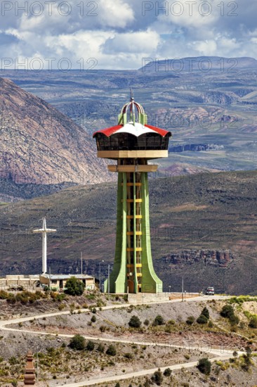 Observation tower on a hill with a cross in front of a mountain range and clouds, The water tower