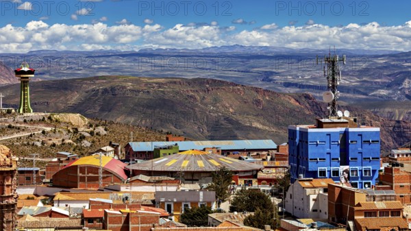 View over a city with colourful roofs and a telecommunications tower, surrounded by mountains under