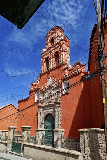 Colonial building with red façade and bell tower, surrounded by power lines and a clear sky, The