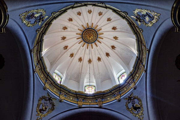 Dome of a church with golden decorations on a blue background and light through windows, inside the