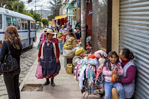Street with vendors, fruit and clothes, busy with passers-by and a bus, people in the streets of