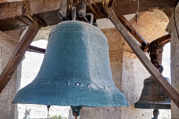Two large bells hang in a historic bell tower with stone pillars and wooden beams, The large bell