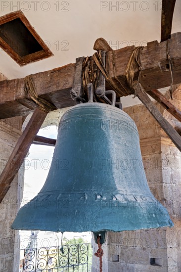 Large bell in an old tower made of wood and stone, with a bright sky in the background, The large
