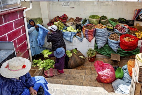 Women arranging vegetables in colourful sacks at a market stall in Bolivia, selling goods in the