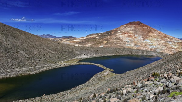 Volcanic mountain reflected in the lake, surrounded by barren landscape and under a bright blue