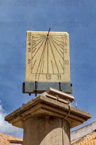 Stone sundial, mounted on a column, with dial and hands in front of a bright sky, The sundial of