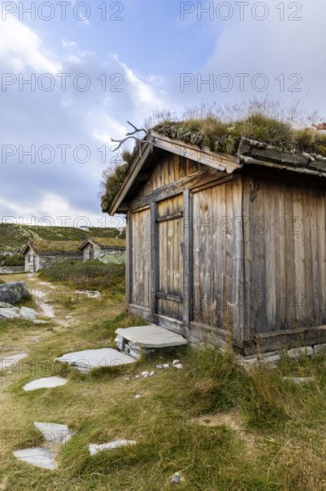 Wooden hut with grass roof and path in a rural setting under a blue sky with clouds, Peer Gynt