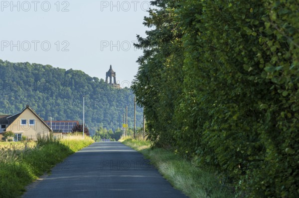 Landscape with a monument on a hill, surrounded by green trees and a house at the roadside,
