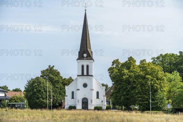 White church with tower and clock, embedded in a green landscape under a blue sky, Herford,