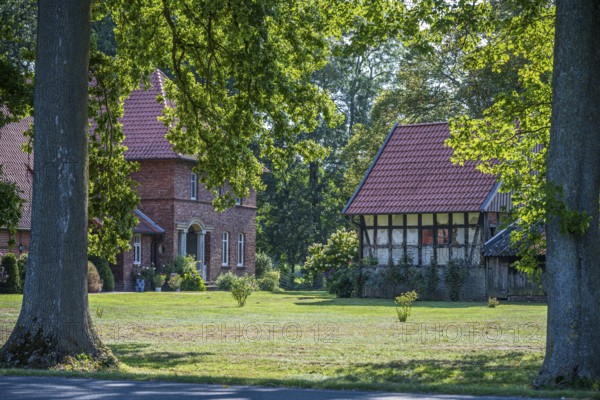 A large tiled roof house next to an older half-timbered building in a green landscape, Gütersloh,