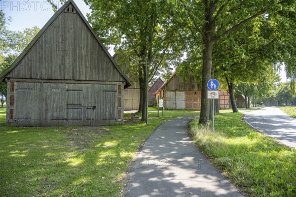 Half-timbered houses next to a cycle path surrounded by green meadows and trees, Weser cycle path,