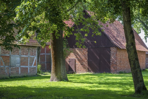 Large brick and wooden barn surrounded by trees and green grass, Weser cycle path, Schlüsselburg