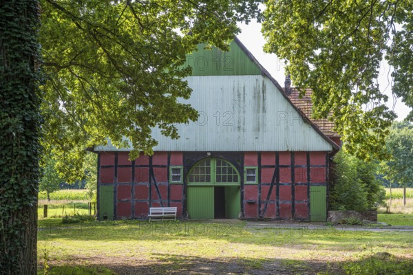 A traditional red and green half-timbered barn surrounded by trees on a sunny day, Gütersloh,