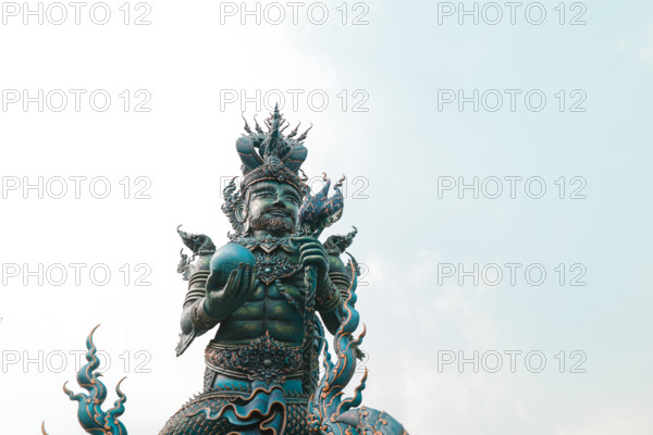 A statue of a mythical figure with intricate details against a pale sky in Wat Rong Suea Ten or