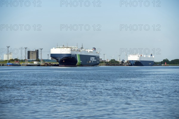 Two large cargo ships moored in the harbour, surrounded by water and blue sky, car freighters in