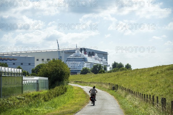 A cyclist on a country road next to a shipyard with a cruise ship in the background, cruise ship at